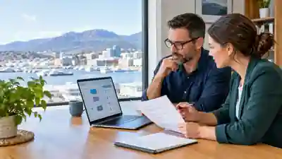 Two business professionals in a Hobart office reviewing an automated decision workflow on a laptop and a printed policy document.